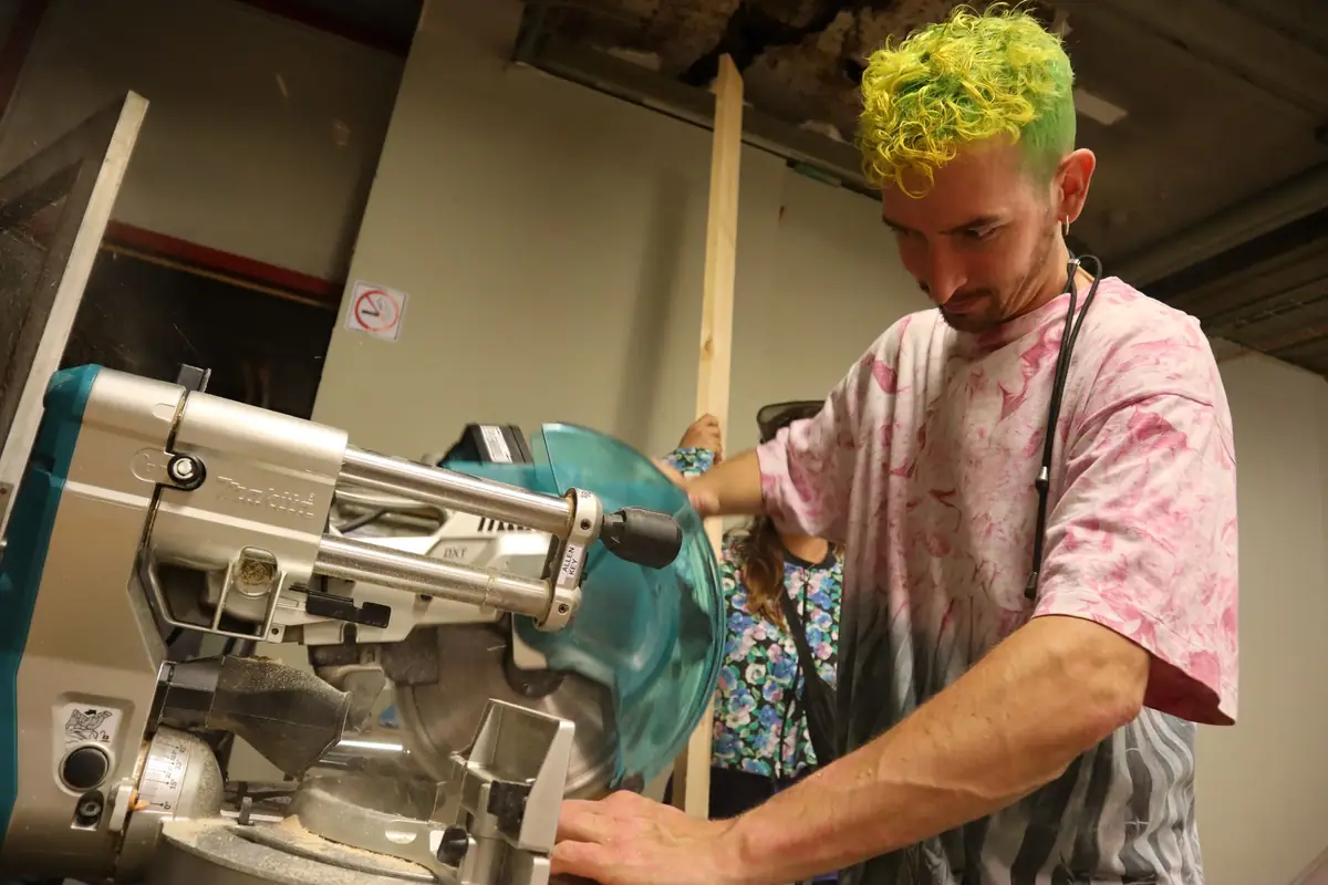 A woodworker cutting a board on a miter saw