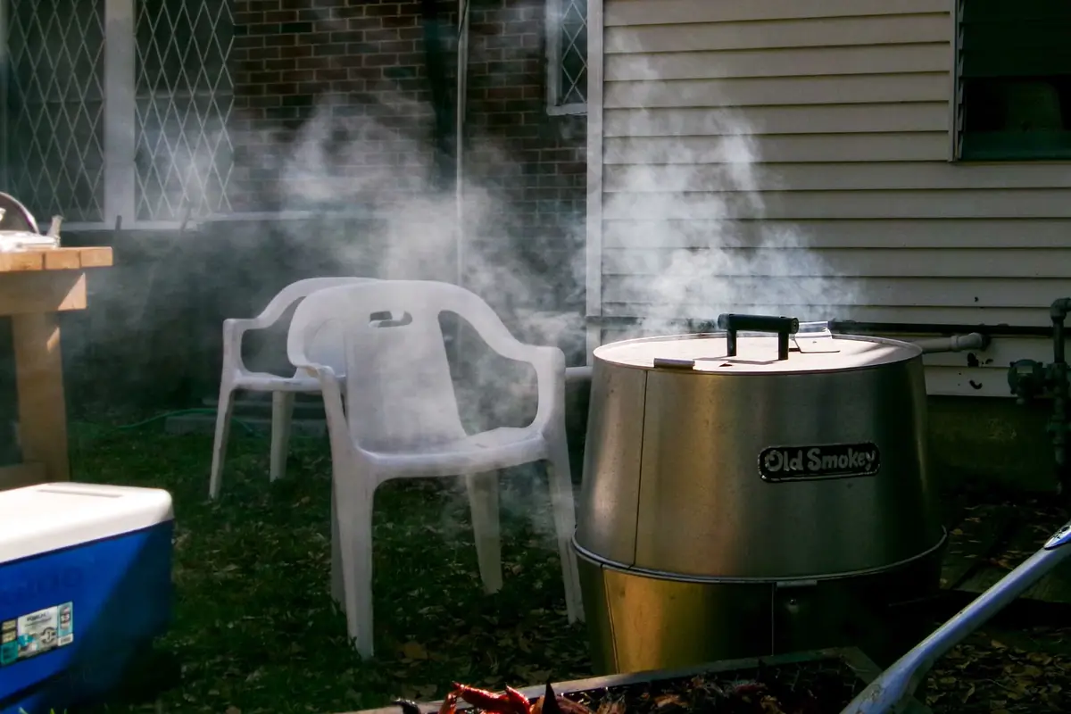A small smoker puffing smoke in a backyard next to plastic chairs