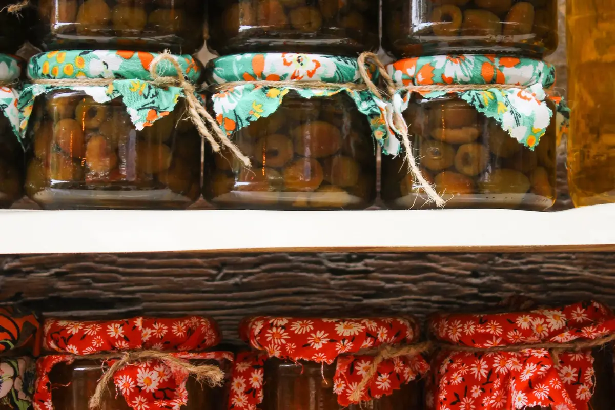 Rows of home-canned jars with fabric-covered lids on a shelf
