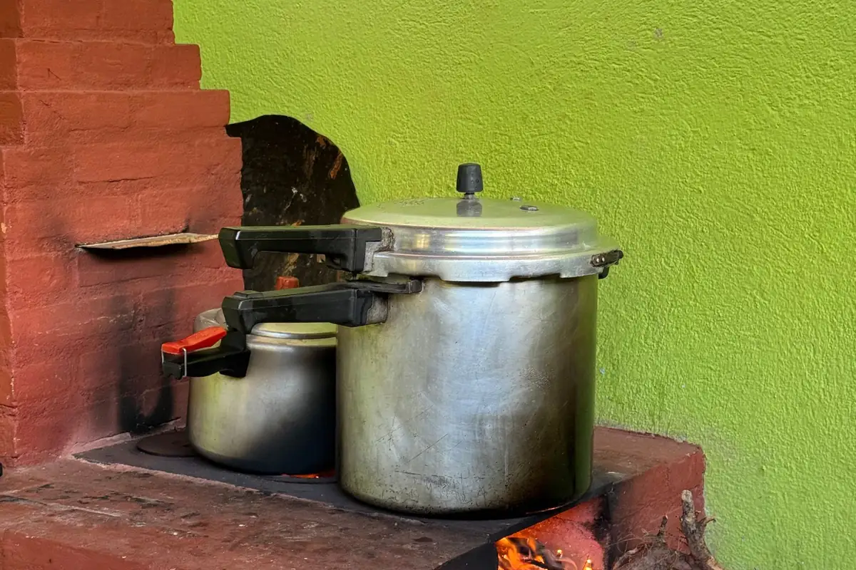 Two stovetop pressure cookers on a brick wood-fired stove