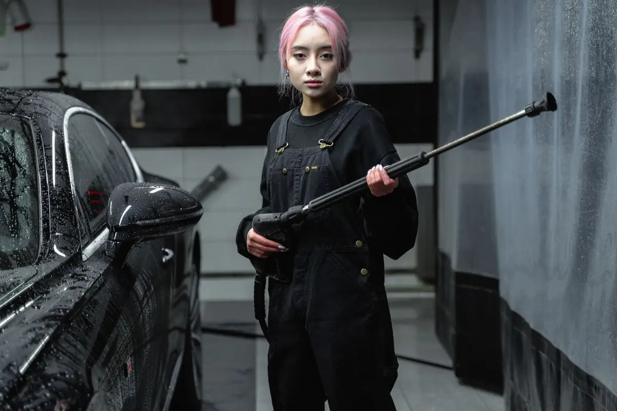 A woman holding a pressure washer wand beside a black car