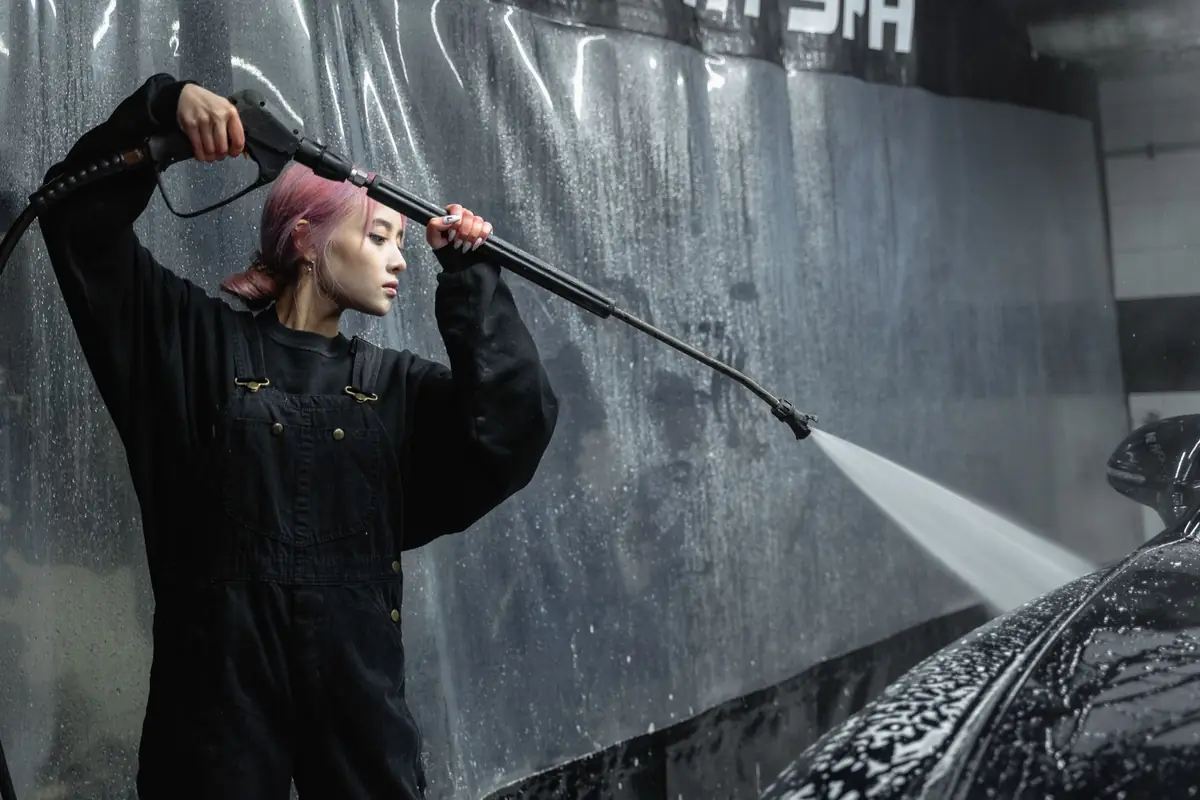 A woman spraying a black car with a pressure washer wand