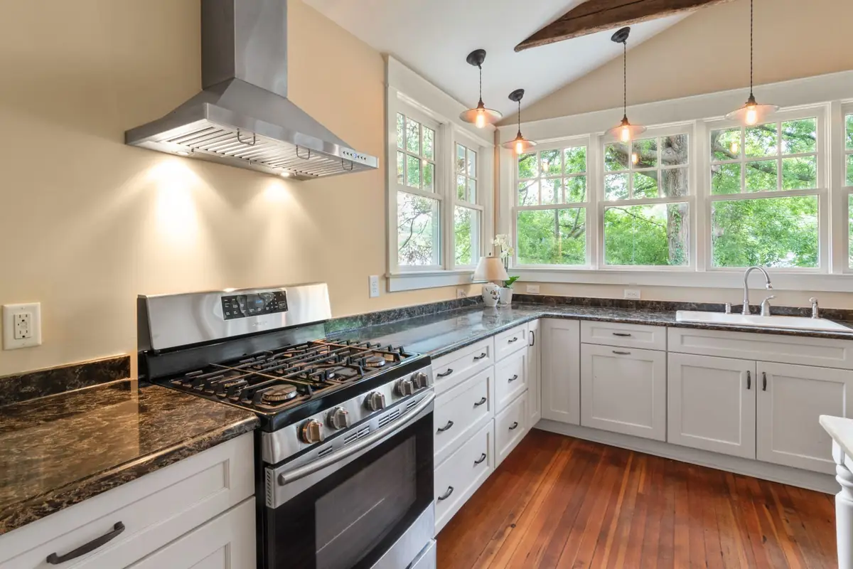 A stainless gas range under a wall-mounted chimney hood