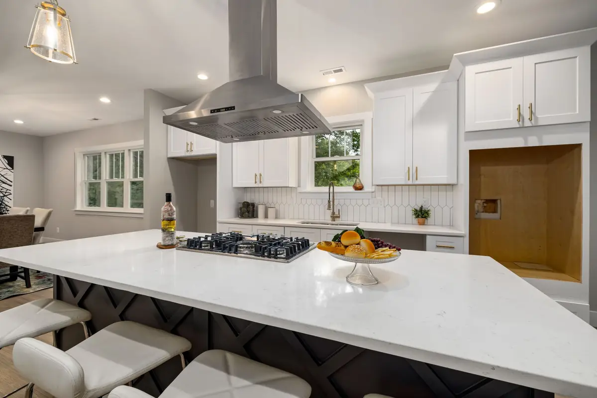 A stainless chimney range hood over a gas cooktop on a white kitchen island