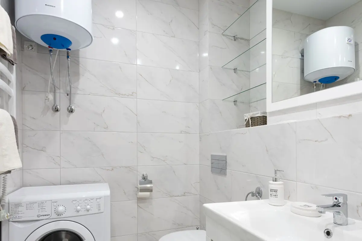 A small bathroom with wall-mounted tank water heaters above a washing machine
