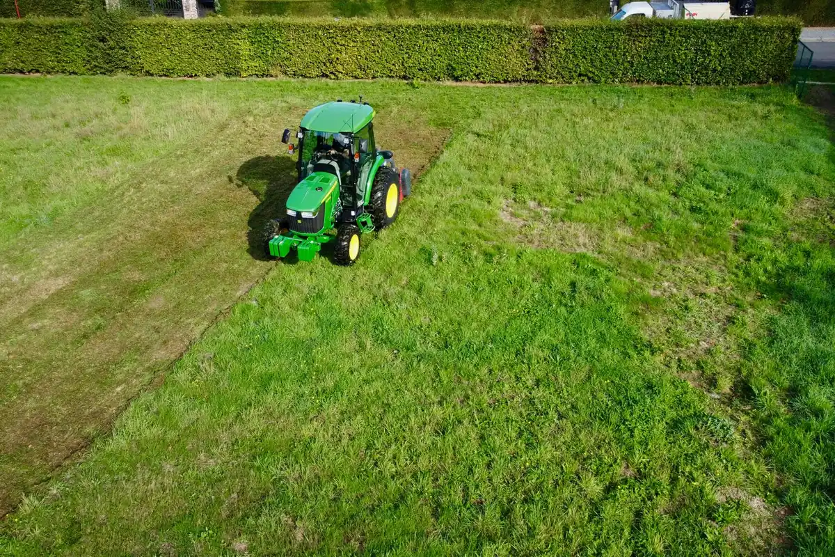 Aerial view of a green lawn tractor cutting stripes into a wide lawn