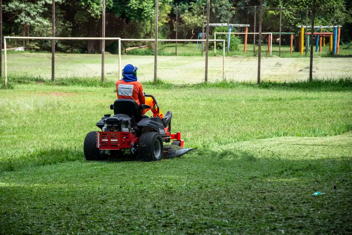 A person on a red riding mower in a large park