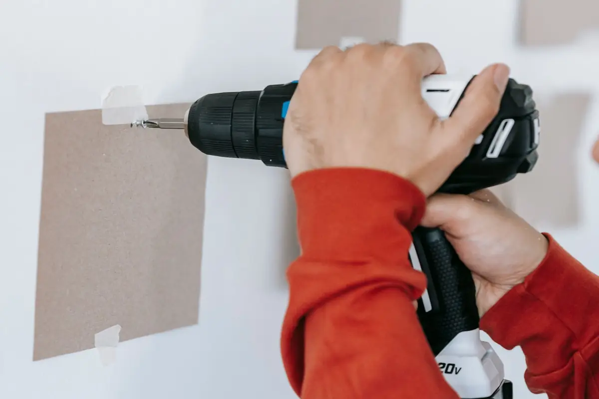 Close-up of hands drilling into a wall with a cordless drill