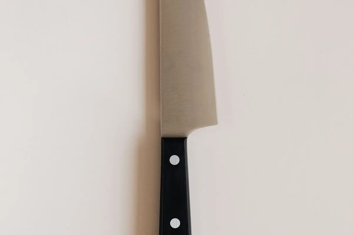 A chef's knife with a black riveted handle on a light countertop