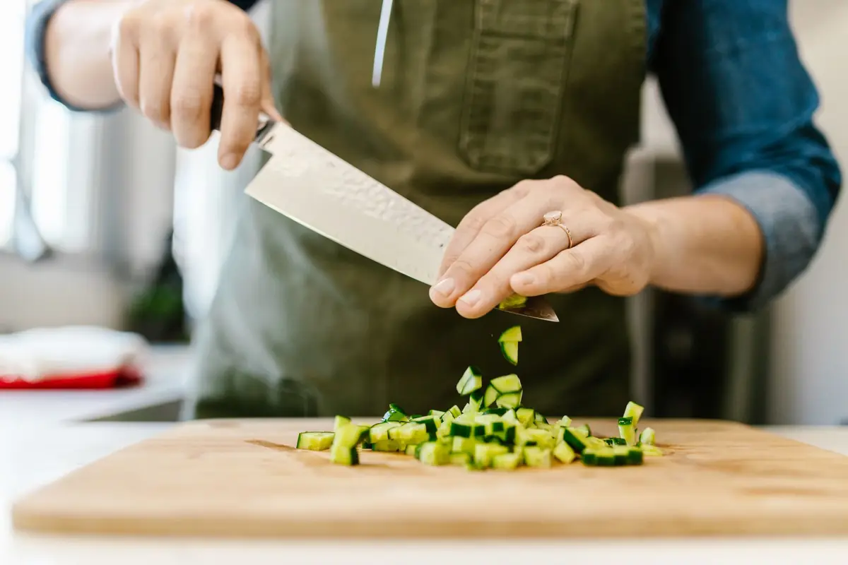 A cook chopping cucumber with a chef's knife on a wooden cutting board